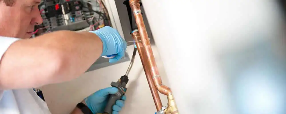 Water heater repair technician testing copper pipe connections and controls in Escondido, CA